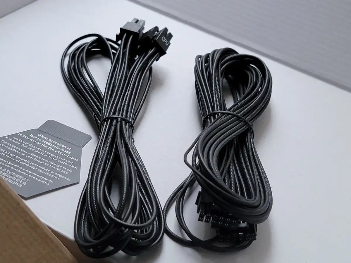 Two neatly coiled black braided computer power cables lie on a white surface, one with a CPU connector and the other with…