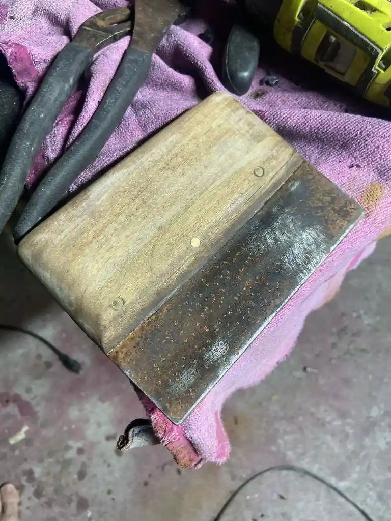 A close-up photo shows the underside of a worn wooden chair with a rusty metal plate, resting on a pink cloth amidst tools…