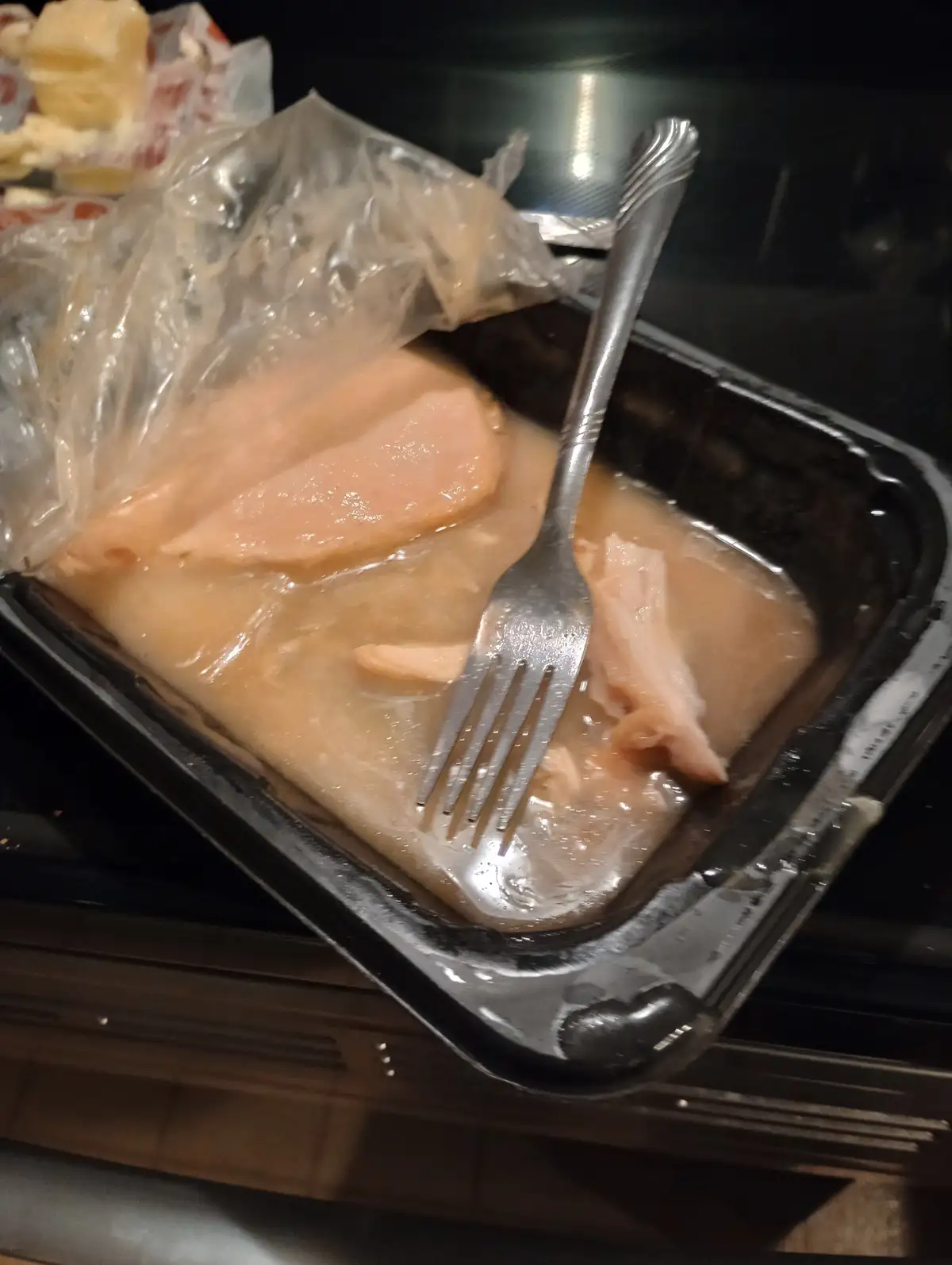 A close-up photo shows a black plastic food container holding soggy, pale pink slices of what appears to be deli meat…