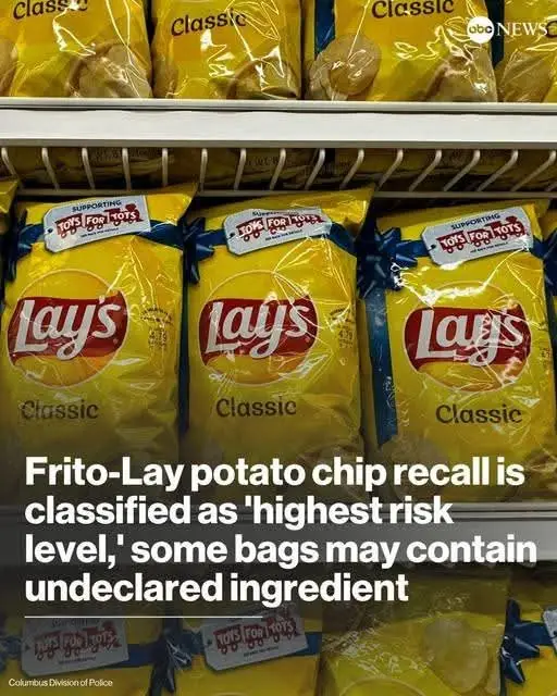 A grocery store shelf displays multiple yellow bags of Lay's Classic potato chips, each adorned with a blue ribbon and a…