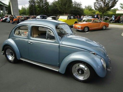A light blue classic Volkswagen Beetle is parked at a car show, with other vintage cars visible in the background. The car…