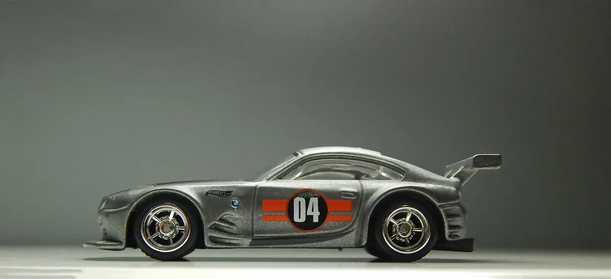 A silver Hot Wheels die-cast model of a BMW Z8 race car is shown in profile against a plain gray background. The car…