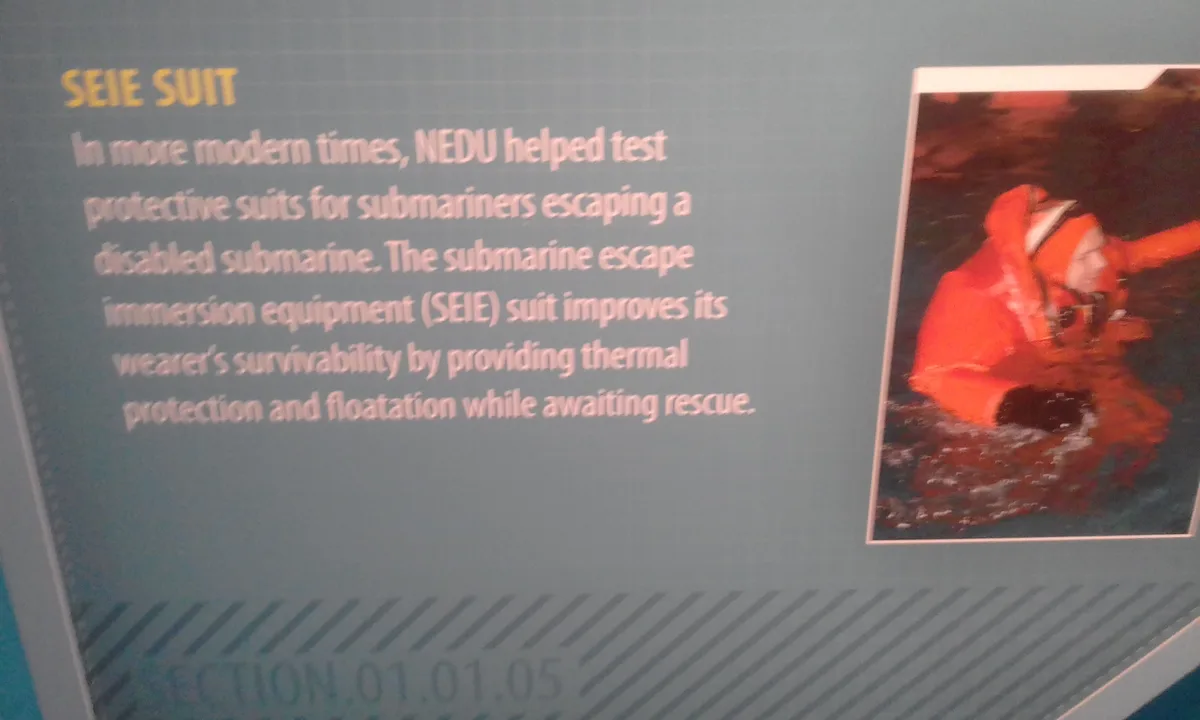 A museum exhibit panel titled 'SEIE SUIT' describes a protective suit for submariners escaping disabled vessels, featuring a…