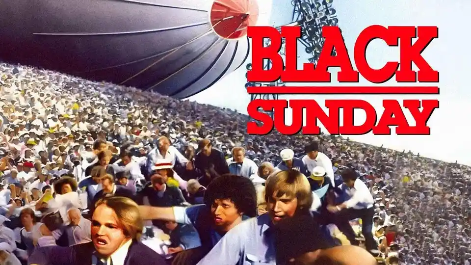 A crowded outdoor scene with a large blimp overhead and a massive crowd of people, overlaid with bold red text reading…
