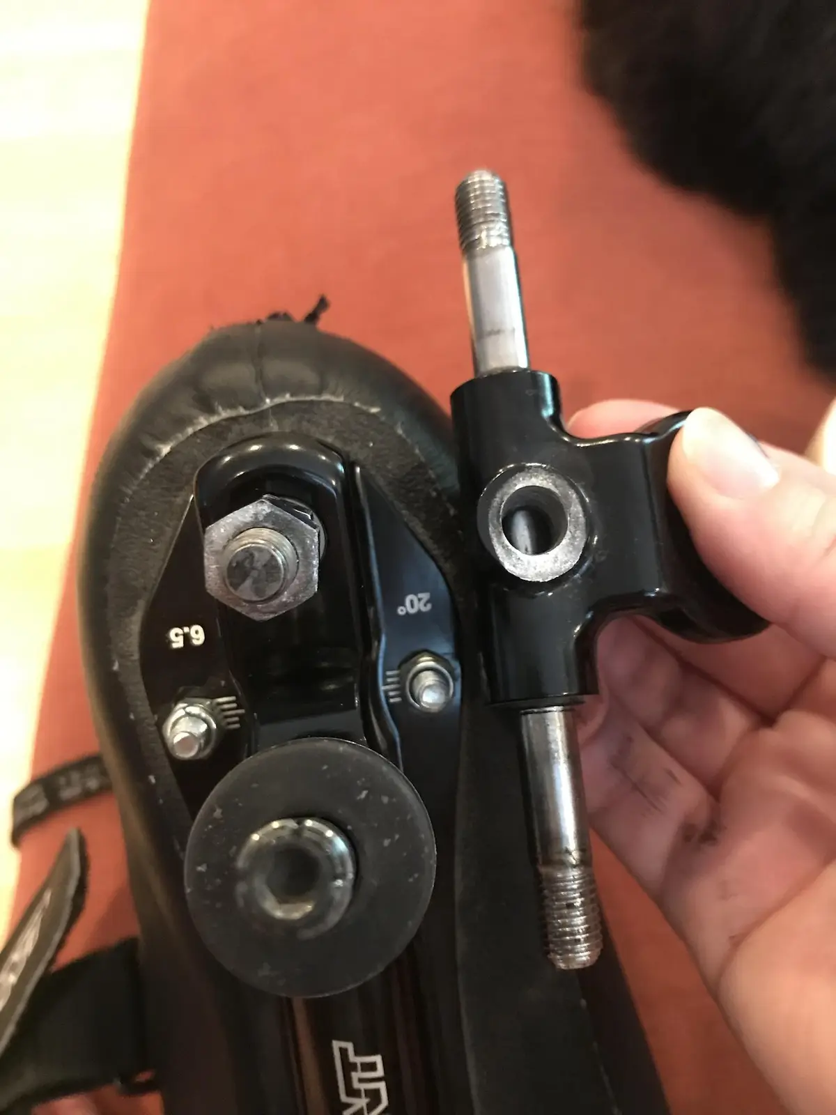 A close-up photo shows a hand holding a black rollerblade boot's adjustable heel piece, which has visible screws, a hex…