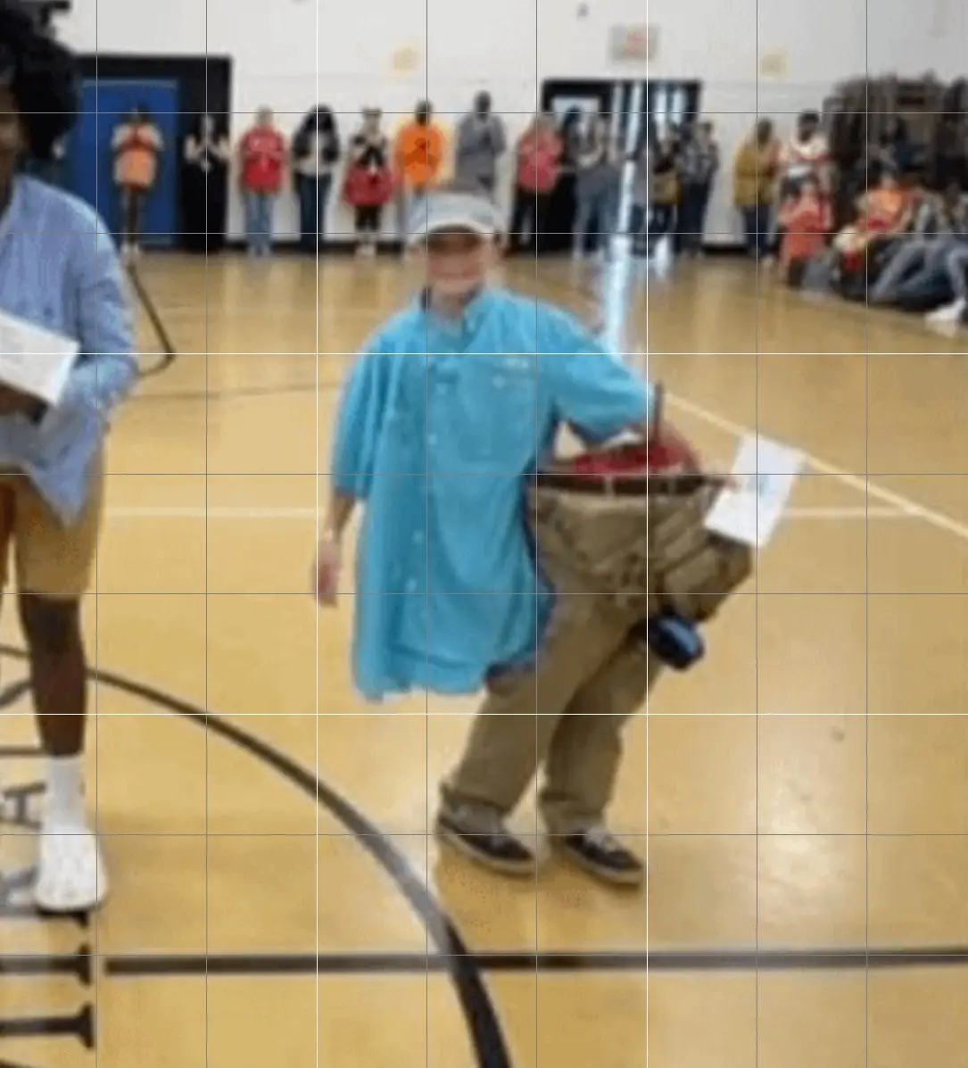 A blurry photo shows a person in a blue shirt and khaki pants walking across a gymnasium floor while carrying a large…