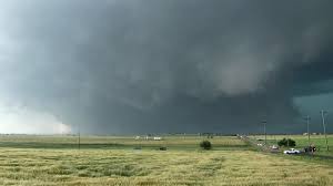 A wide, flat grassy field under a massive, ominous dark storm cloud that appears to be a tornado forming on the horizon…