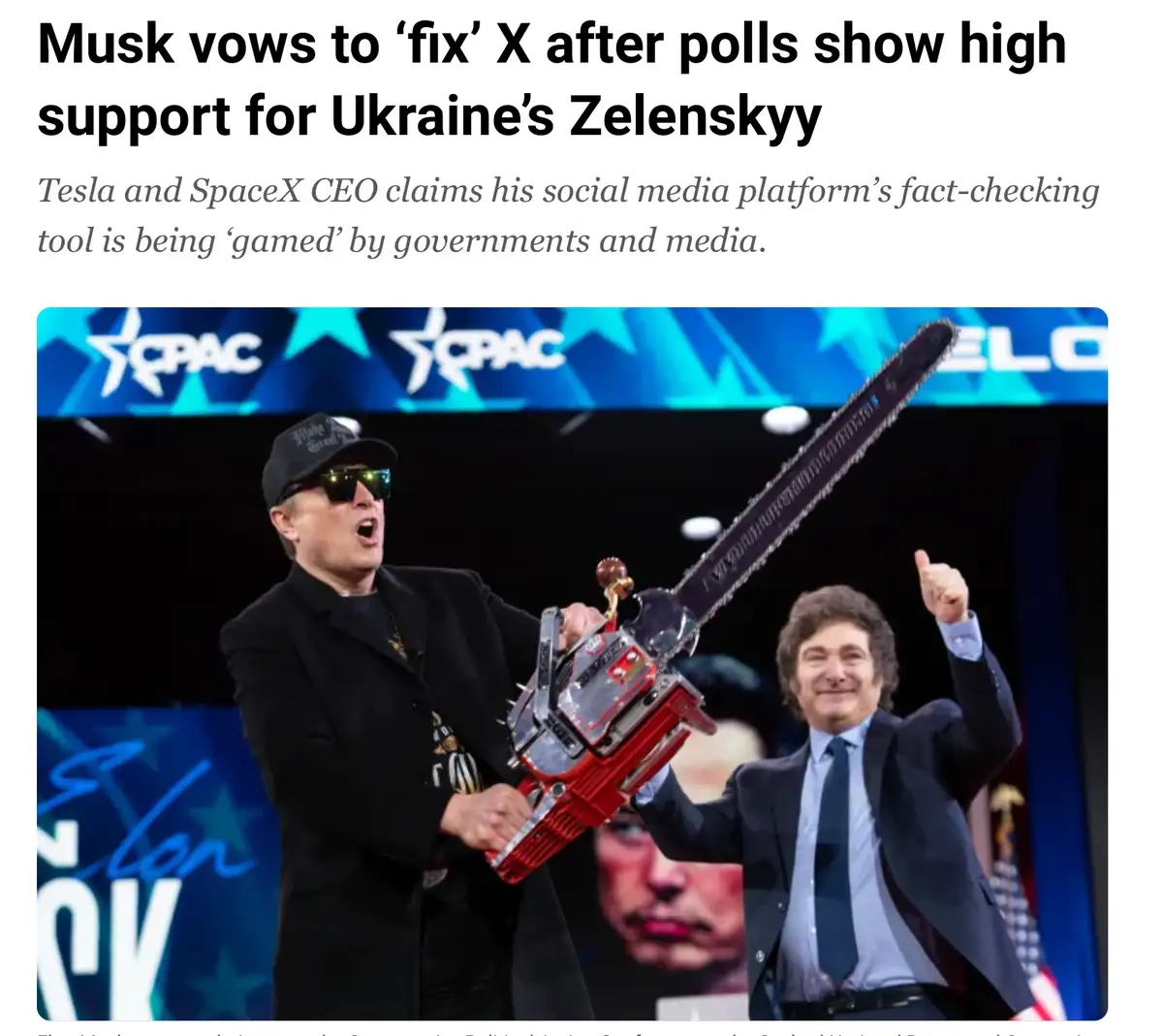 A man in a black jacket and cap holds a large chainsaw while another man in a suit gives a thumbs-up. The image is overlaid…