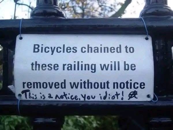 A white sign on a black metal railing reads 'Bicycles chained to these railing will be removed without notice,' with…