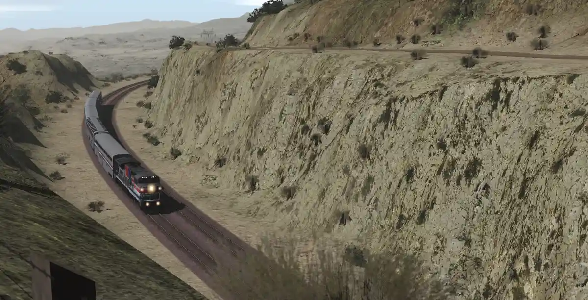 A train with a locomotive and passenger cars travels along a curving track through a desert canyon, with steep, rocky cliffs…
