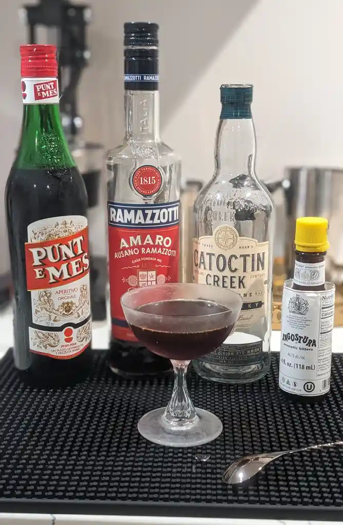a close-up photo shows a cocktail in a coupe glass surrounded by its four ingredient bottles: punt e mes, ramazzotti amaro…