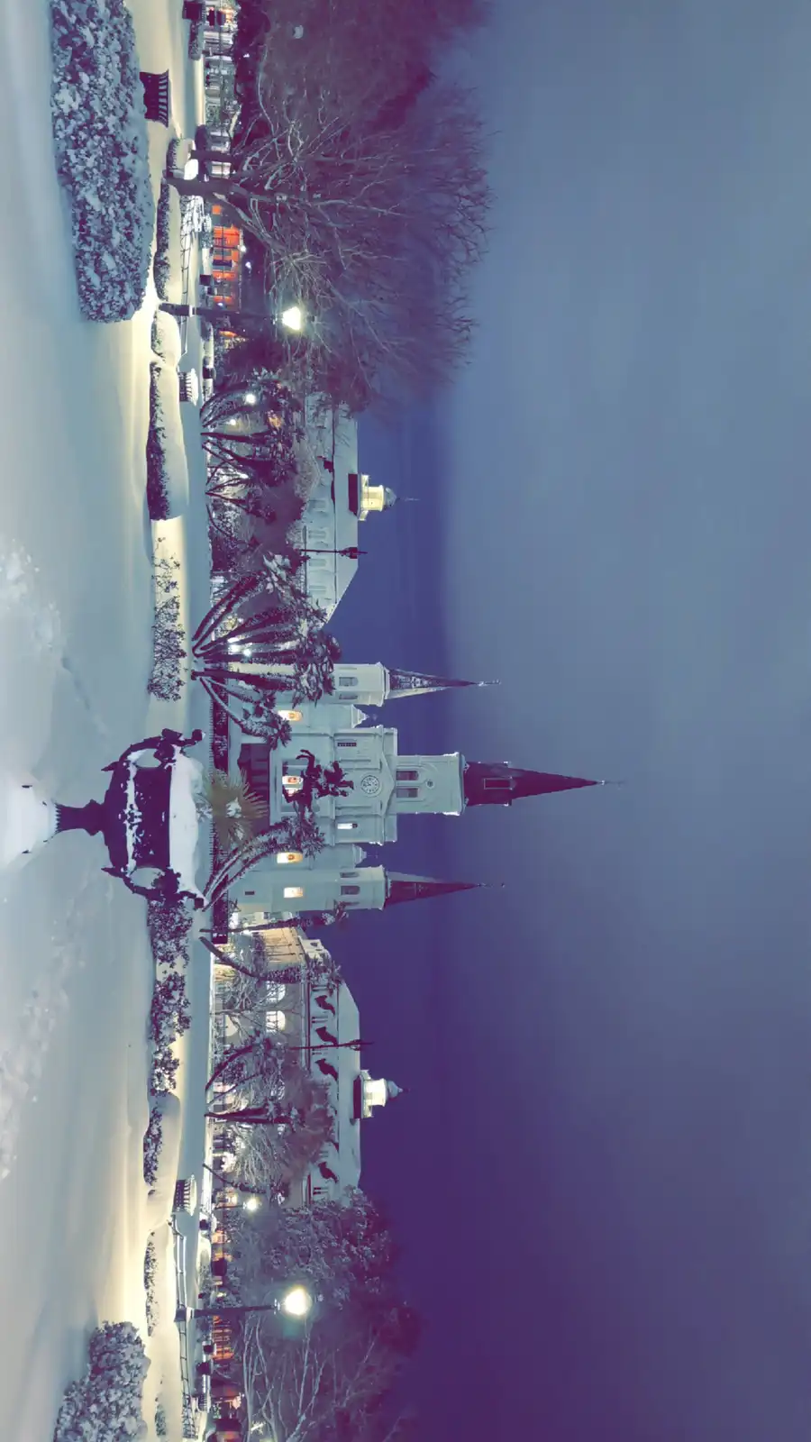 A vertically oriented image shows a snowy scene in New Orleans, featuring a prominent church with multiple spires and…