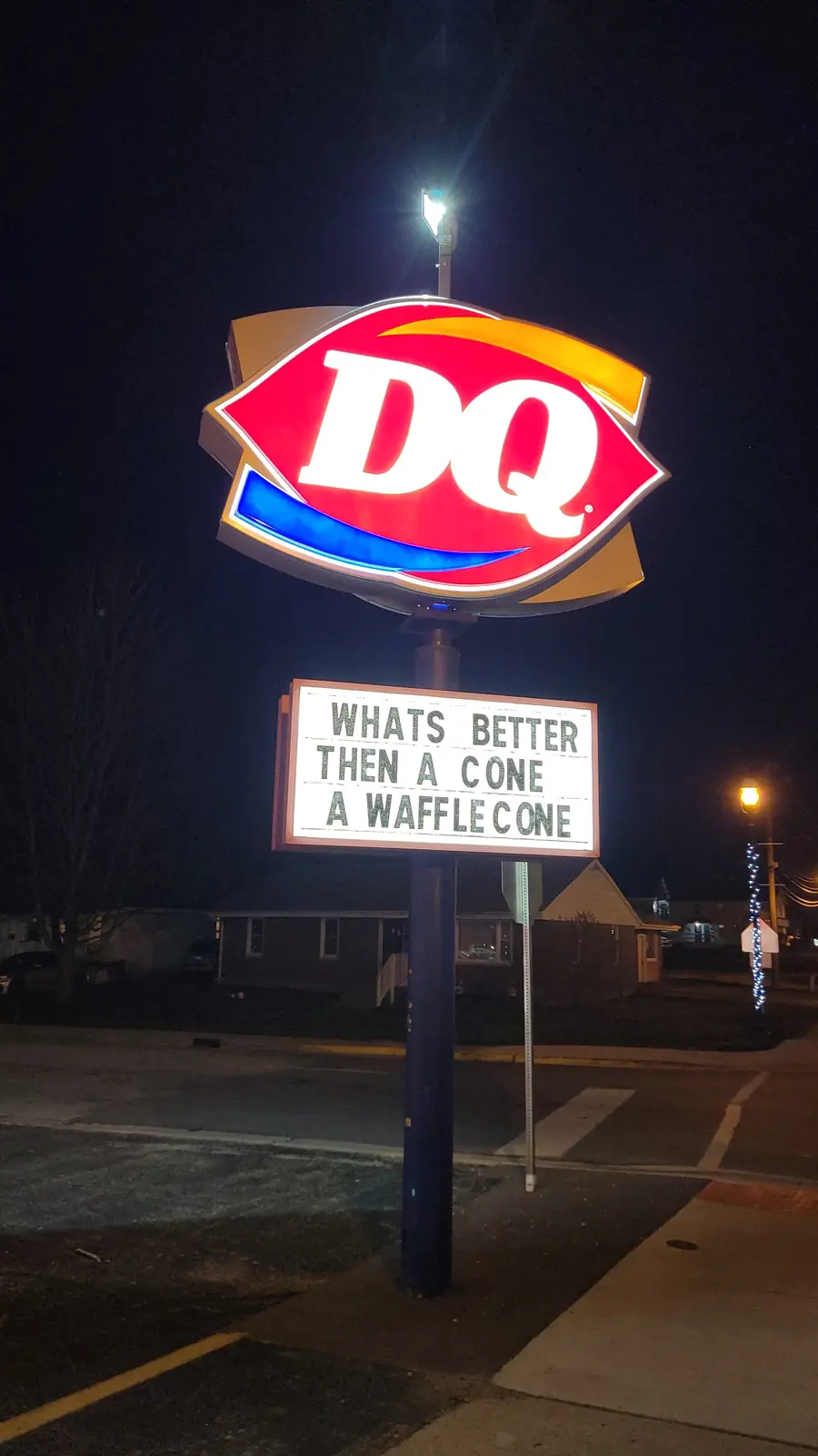 A nighttime photo of a brightly lit Dairy Queen sign with a marquee below it that reads 'WHATS BETTER THEN A CONE A WAFFLE…