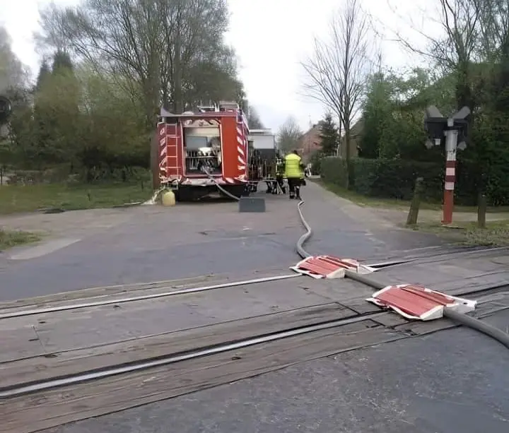 A red fire truck is parked on a street with tram tracks running through it. Firefighters in yellow uniforms are visible near…