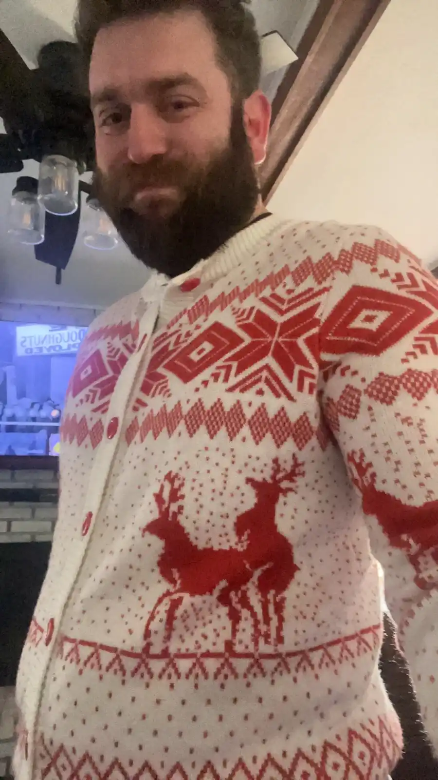 a man with a beard wears a white and red holiday sweater featuring reindeer and geometric patterns. The overlaid text reads…