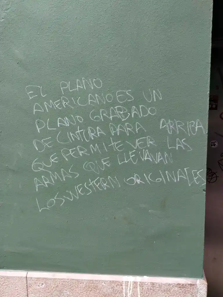 A green-painted wall has white chalk writing in Spanish that reads 'El plano americano es un plano grabado de cintura para…