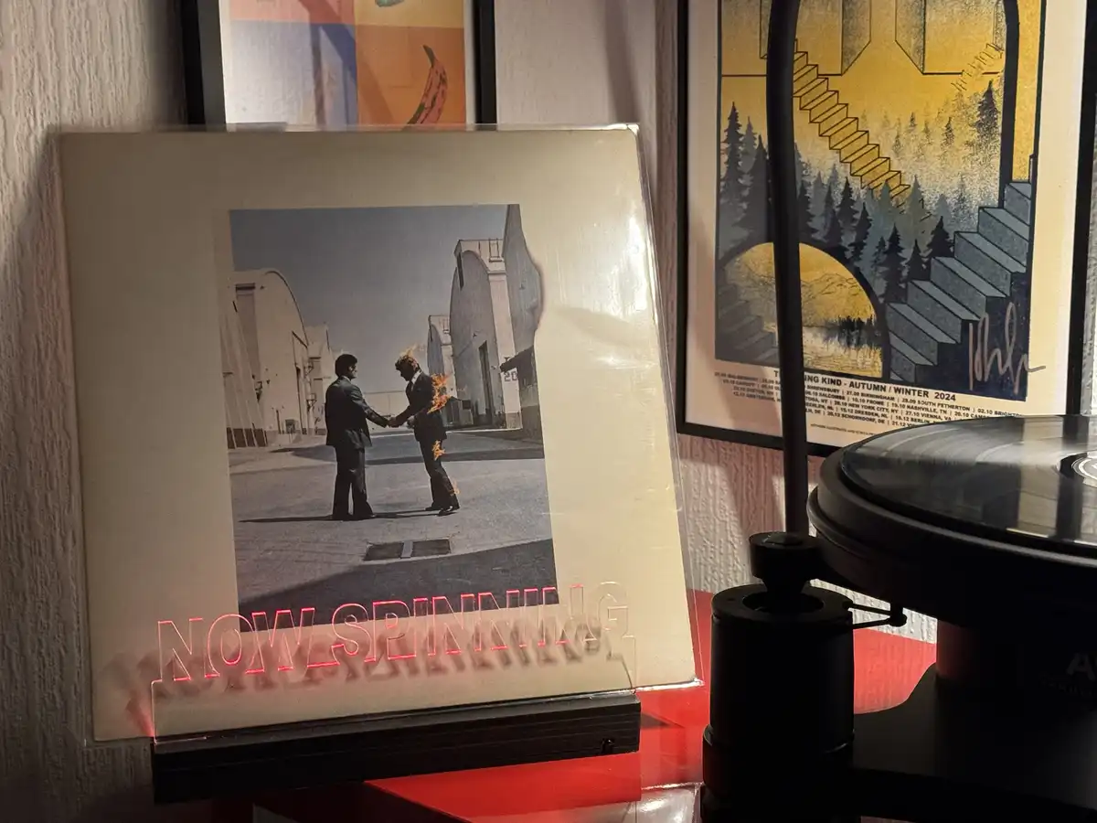 A vinyl record sleeve featuring two men shaking hands, one of whom is on fire, is displayed on a red surface next to a…