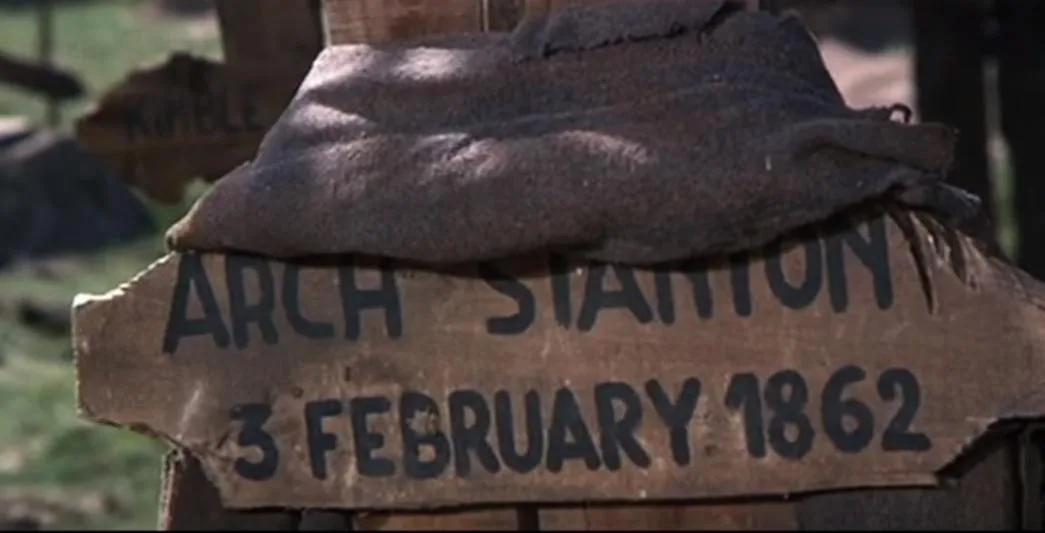 A close-up of a weathered wooden grave marker with the name 'ARCH STANTON' and the date '3 FEBRUARY 1862' painted in black…