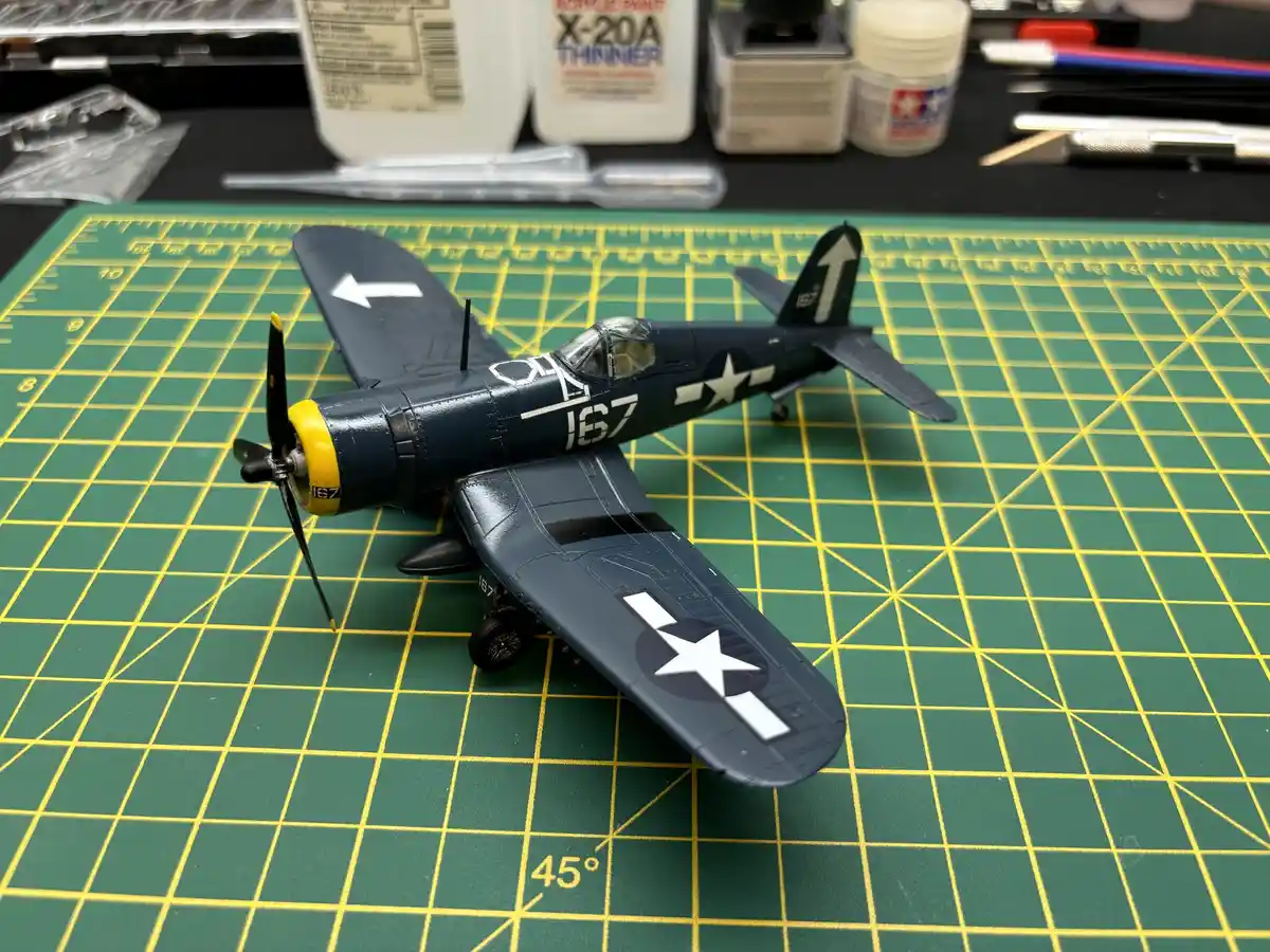A detailed scale model of a dark blue U.S. military fighter plane, marked with the number 167 and white star insignia, sits…