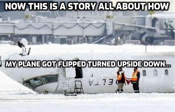 An airplane is shown upside down in a snowy airport environment, with its nose pointing toward the sky and its tail touching…