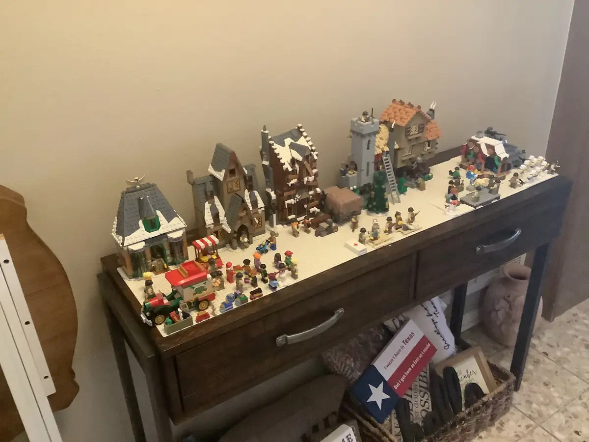 A detailed LEGO diorama of a snowy village with multiple buildings, minifigures, and a Christmas tree sits on a dark wooden…
