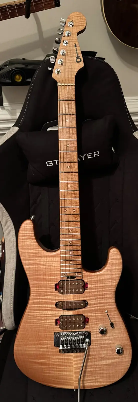 A light-colored electric guitar with a prominent wood grain pattern is propped upright in a black guitar case. The case has…