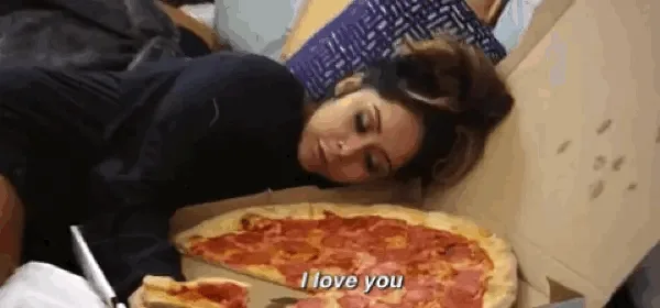 A woman is shown lying down with her head resting on the edge of a large open pizza box, appearing to be asleep or very…