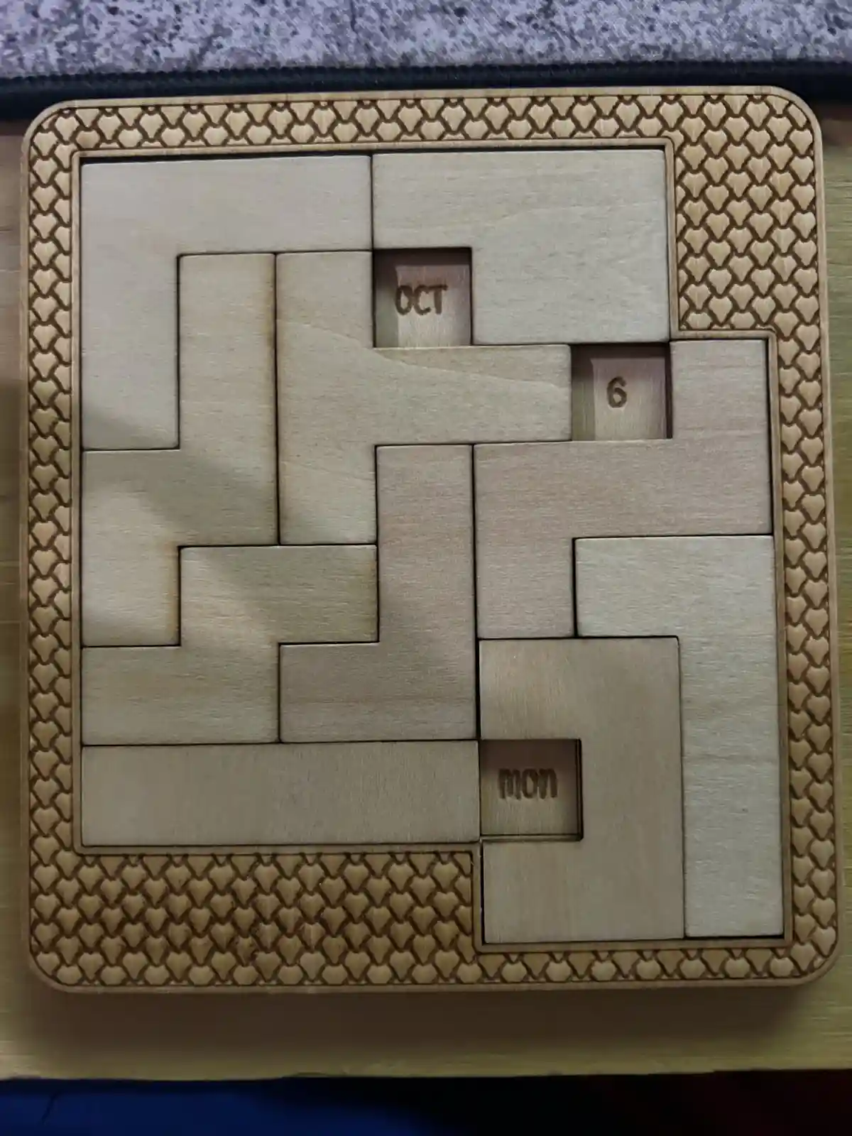 A wooden puzzle calendar with interlocking pieces, where three small blocks reveal the text 'OCT', '6', and 'MON', arranged…