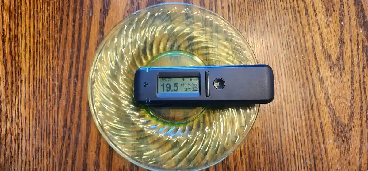 A black digital device with a screen displaying '19.5', '±13%', and 'CPS' rests on a clear, ribbed glass plate atop a wooden…