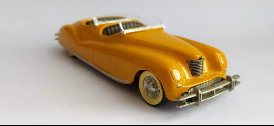 A yellow die-cast model of a vintage convertible car with a silver roof rack and chrome details, photographed against a…
