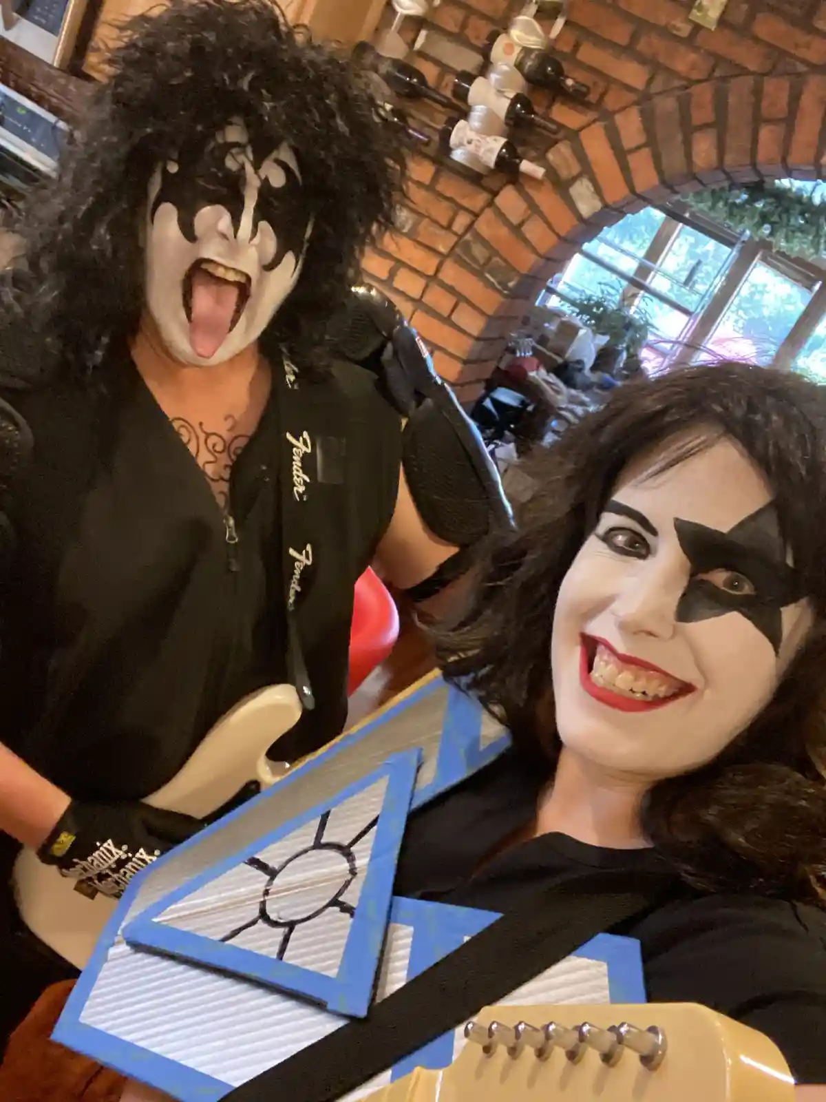 Two people dressed as Kiss band members, one with a classic black and white face paint and tongue out, the other with a…