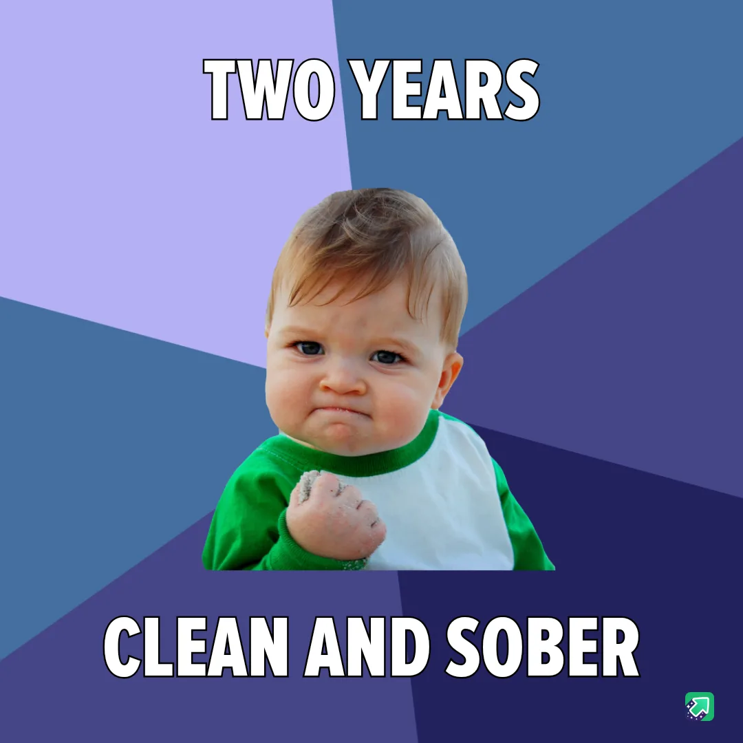 A baby with a determined, slightly smug expression, wearing a green and white shirt, clenches a fist with sand on it. The…