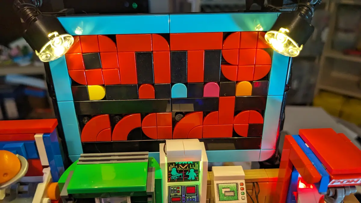 A close-up of a LEGO diorama featuring a large screen made of red, black, and colored LEGO bricks displaying the word 'dits'…