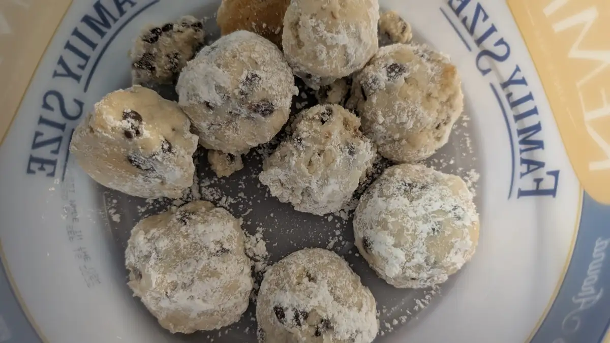 A close-up photo shows several undecorated, flour-dusted cookie dough balls on a white plate with blue lettering that reads…