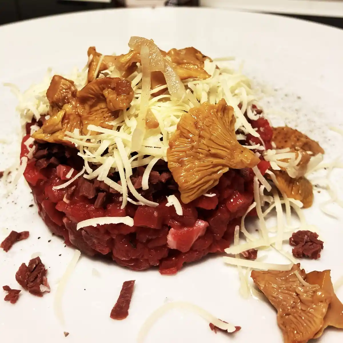 A close-up photo of a gourmet dish on a white plate, featuring a mound of finely chopped red meat, likely beef tartare…