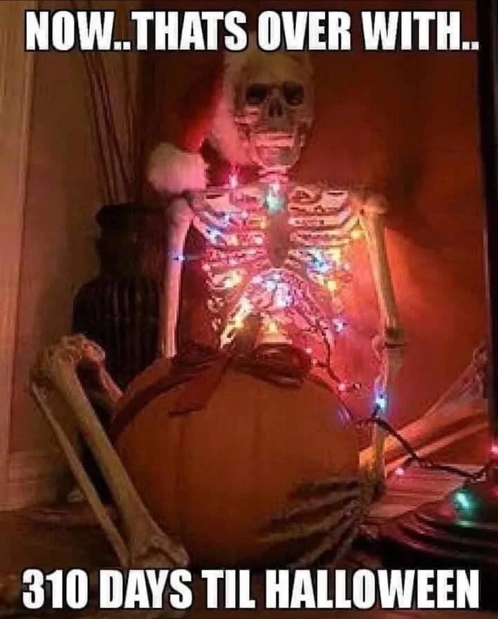 A skeleton wearing a Santa hat sits in a chair with a large pumpkin on its lap, illuminated by colorful string lights inside…