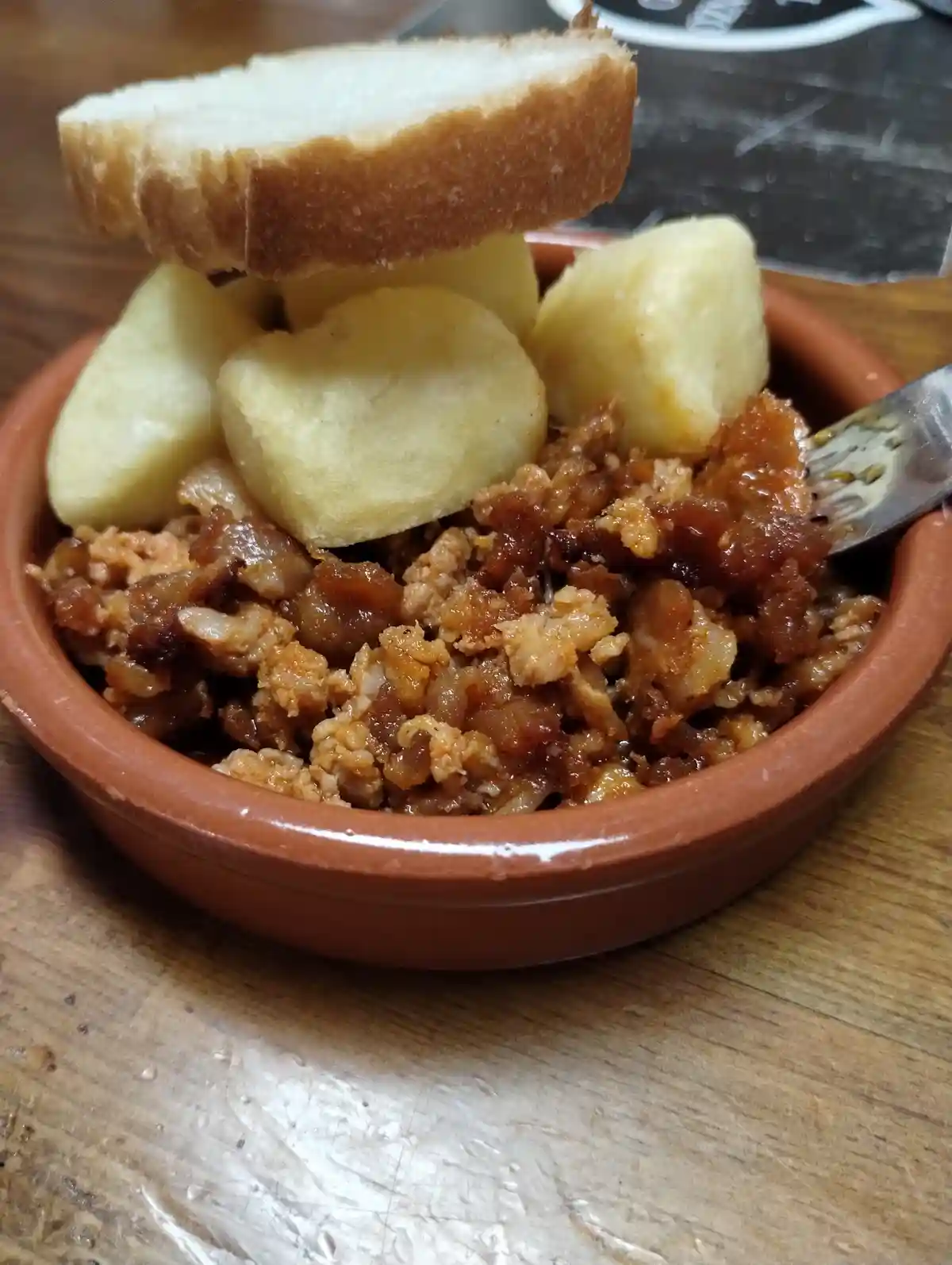 A close-up photo shows a traditional Spanish dish, likely fabada or similar, served in a terracotta bowl. The dish contains…