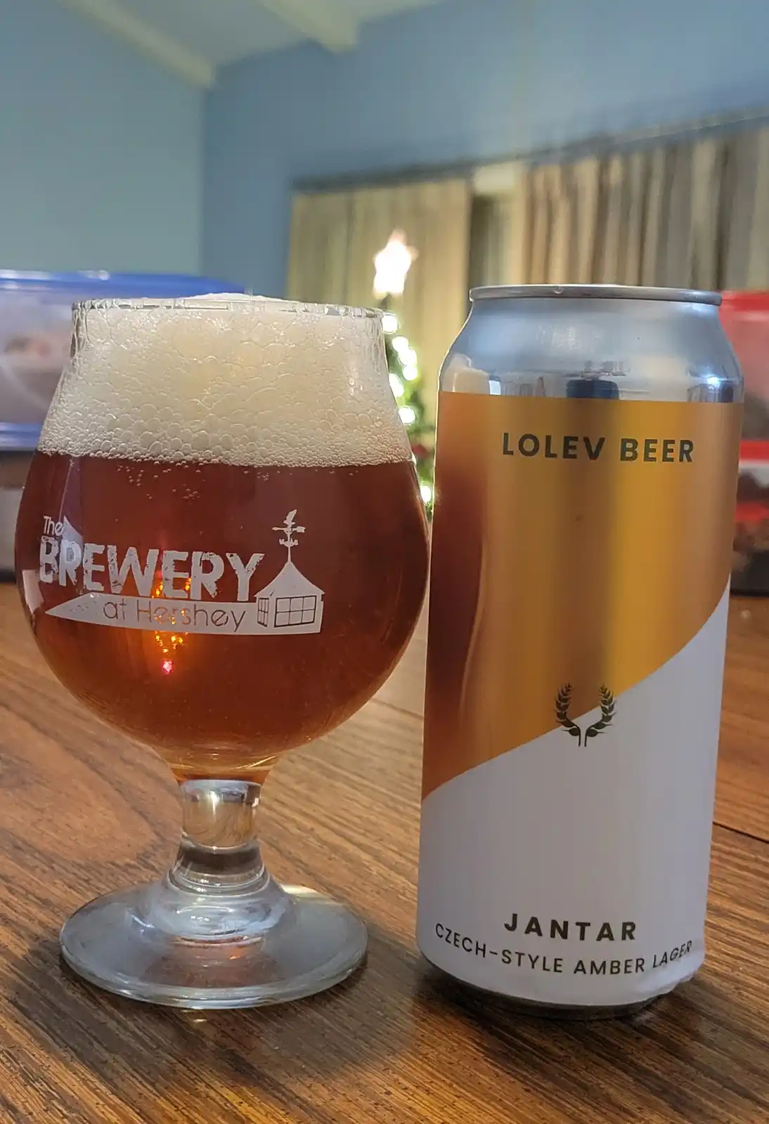 A can of Lolev Beer Jantar Czech-Style Amber Lager sits next to a glass filled with amber beer and a thick white head, both…