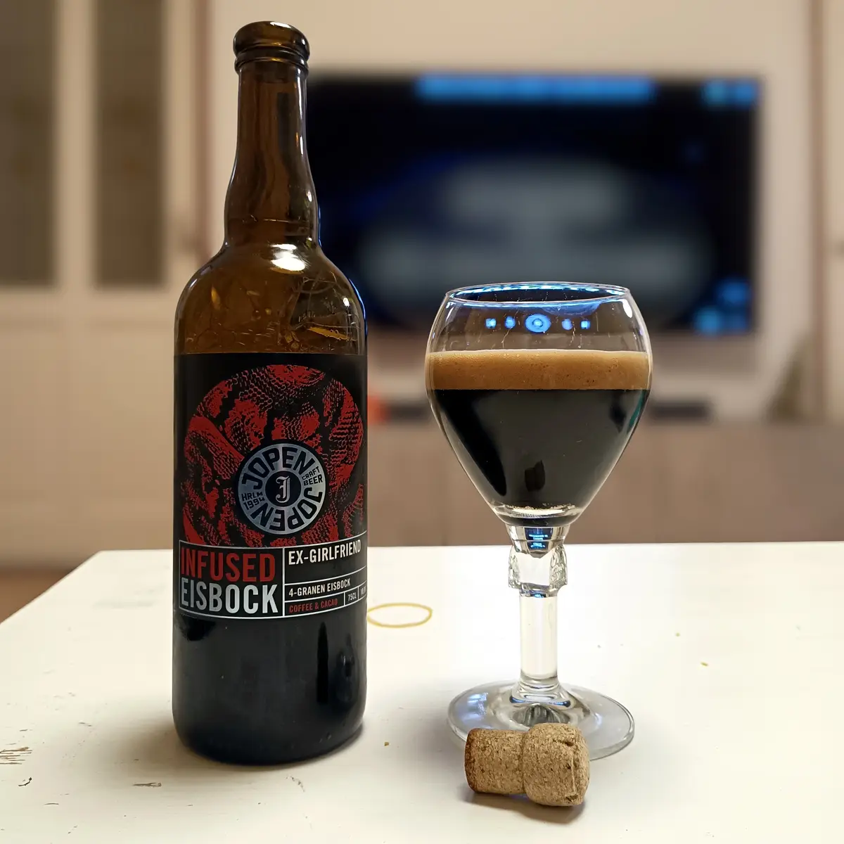 A brown bottle of Jopen craft beer labeled 'INFUSED EISBOCK EX-GIRLFRIEND' sits next to a glass filled with dark beer and a…