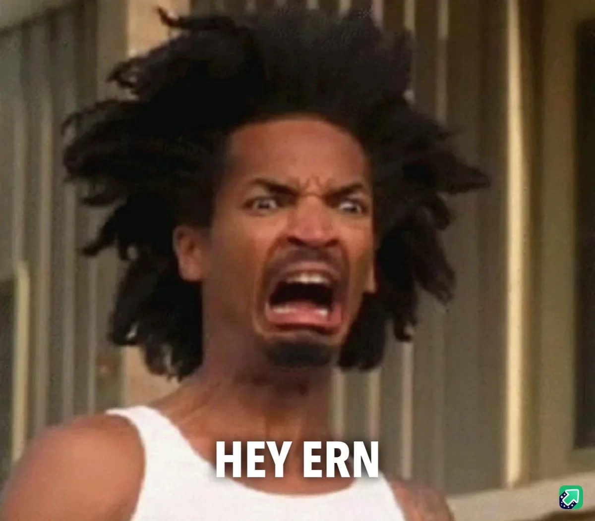 A man with wild black dreadlocks and a white tank top is captured mid-shout with an intense, angry expression, his mouth…