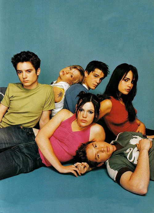A promotional photo of the cast of 'The O.C.' lying on a blue floor, all looking directly at the camera with serious…