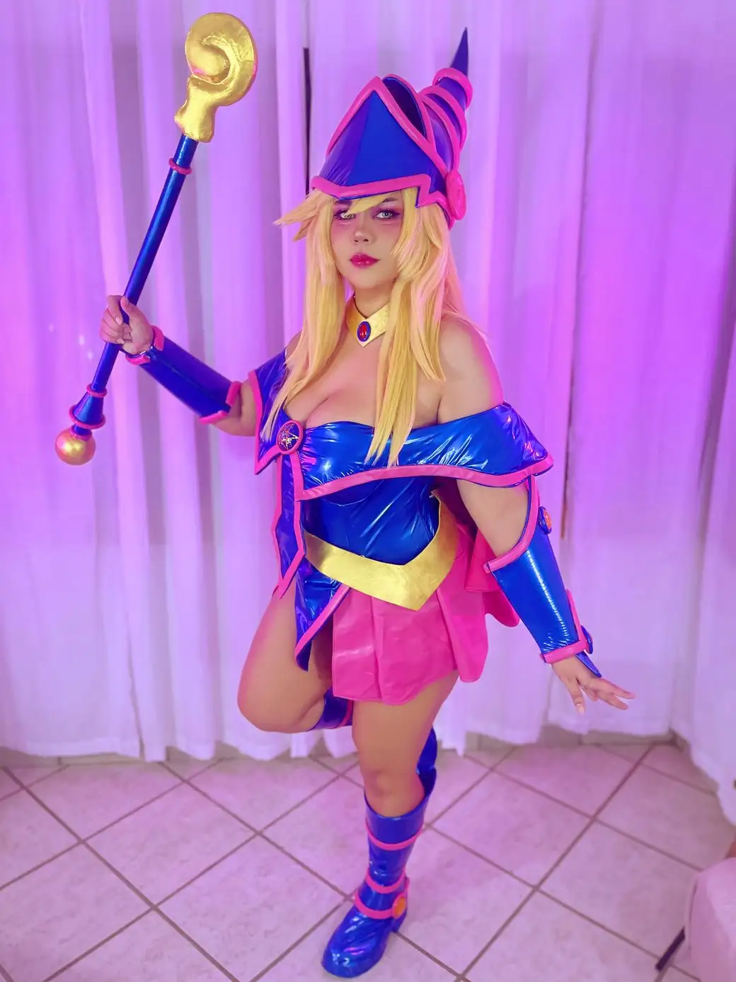 A person in a detailed cosplay of the character Yugi Muto's Dark Magician Girl from Yu-Gi-Oh!, holding her iconic staff…