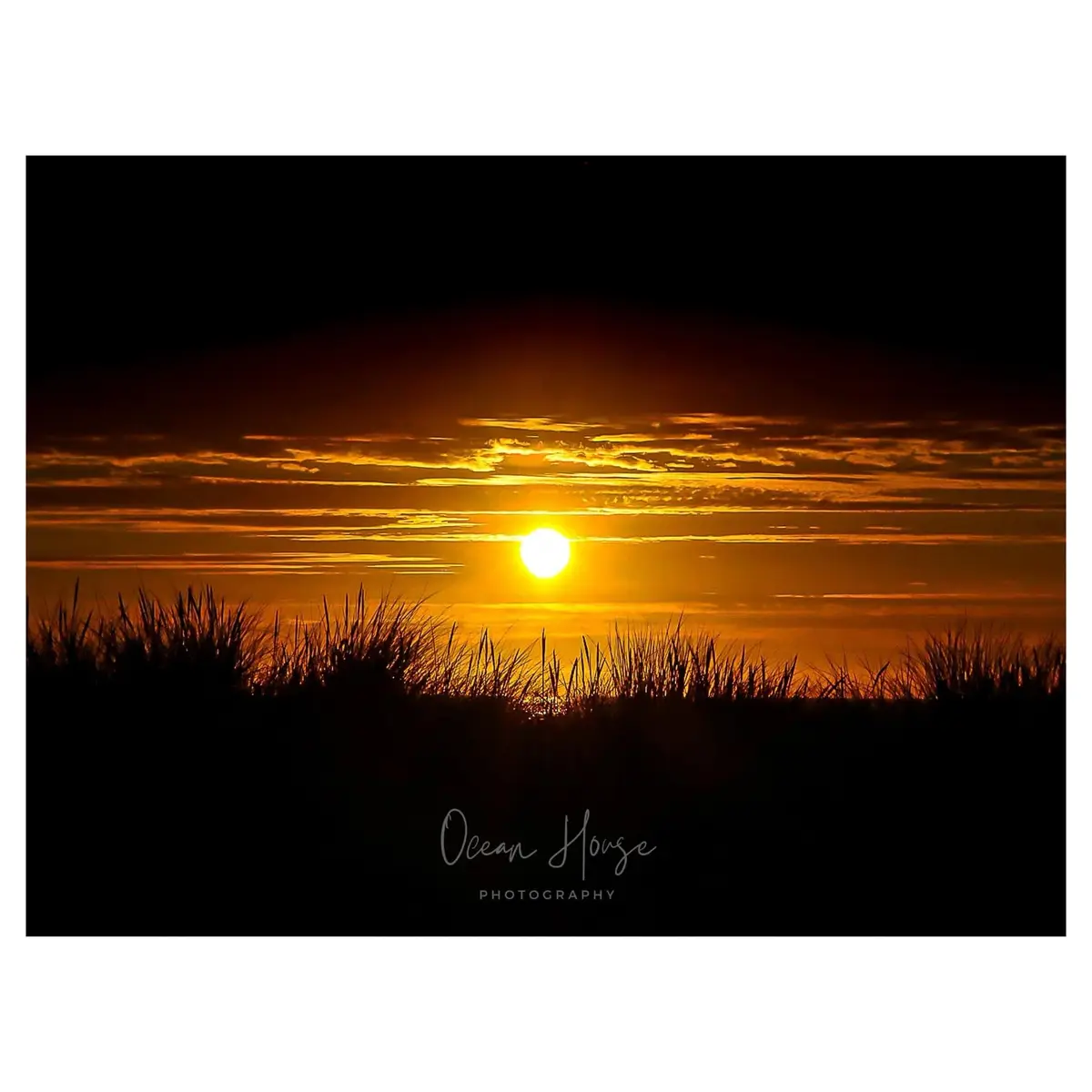 A serene sunset photograph shows a bright orange sun setting over a horizon with layered clouds, framed by dark silhouettes…