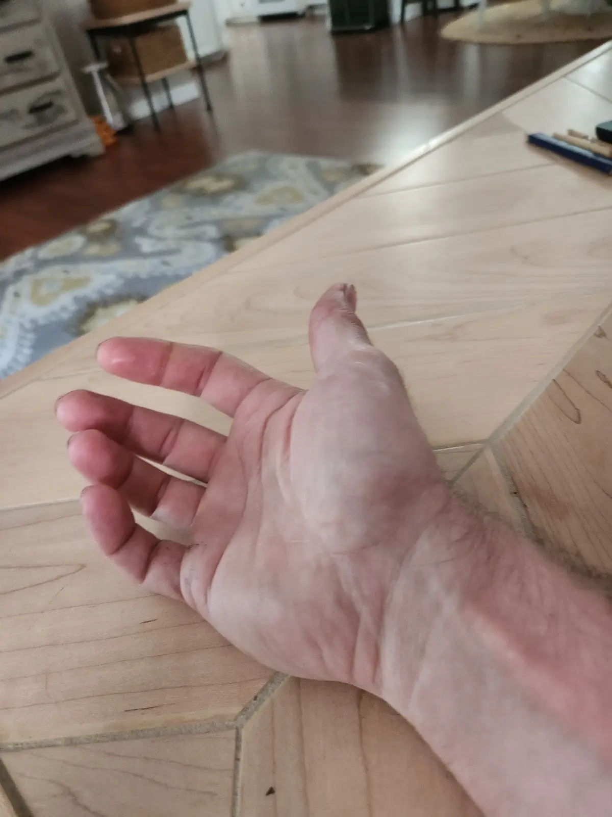 A close-up shot of a person's hand resting on a light-colored wooden surface, likely a table or workbench, with a blurred…