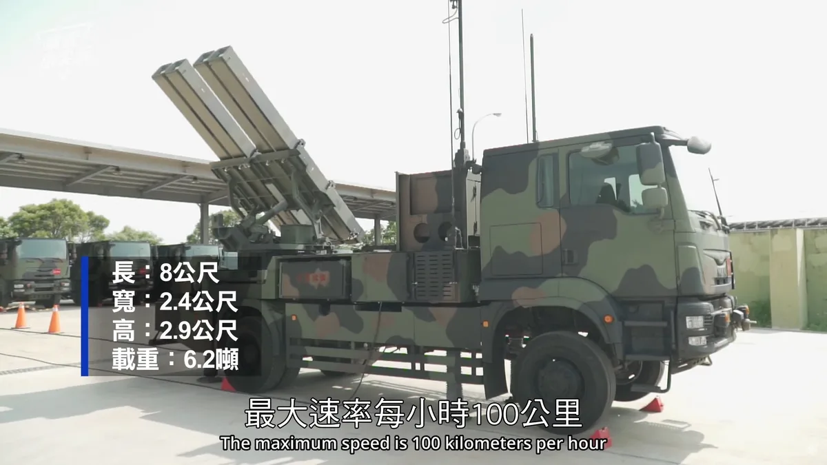 A military truck with a mounted missile launcher is shown parked under a shelter. On-screen text lists its dimensions…