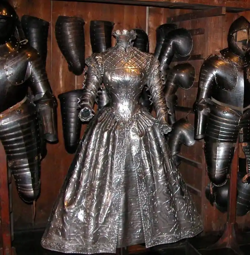 a full-length, ornate dress crafted entirely from metal armor plates is displayed on a mannequin, flanked by traditional…