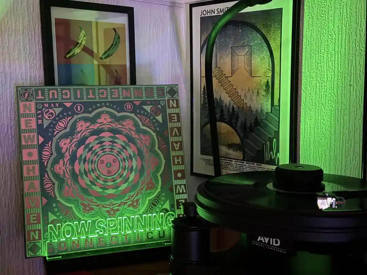 A vinyl record player with a glowing green neon sign that reads 'NOW SPINNING CONNECTICUT' is positioned next to framed…