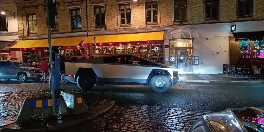 a silver tesla cybertruck with its distinctive angular, futuristic design is parked on a wet cobblestone street at night…