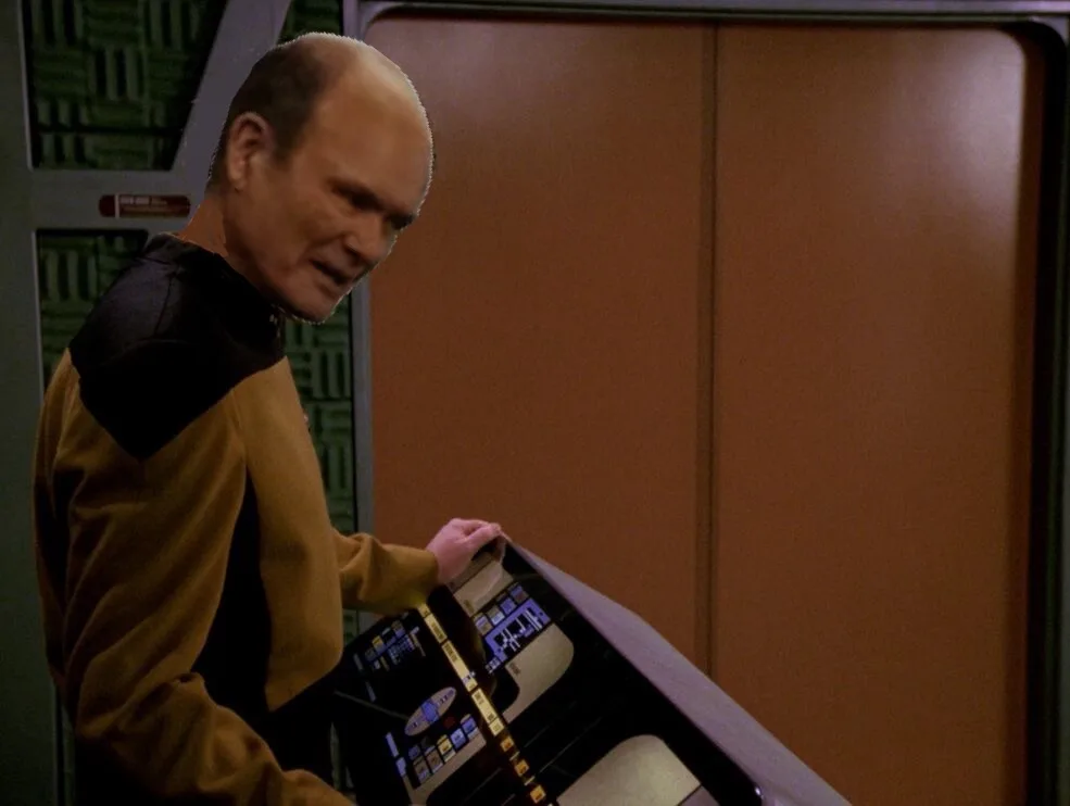 A man in a Star Trek uniform with a bald head and a stern expression is holding a futuristic console. The overlaid text…