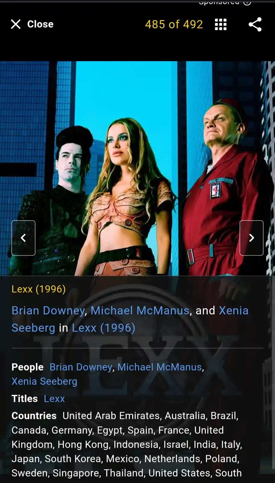 The image shows three actors from the 1996 sci-fi series 'Lexx' standing against a blue-lit futuristic city backdrop. Brian…
